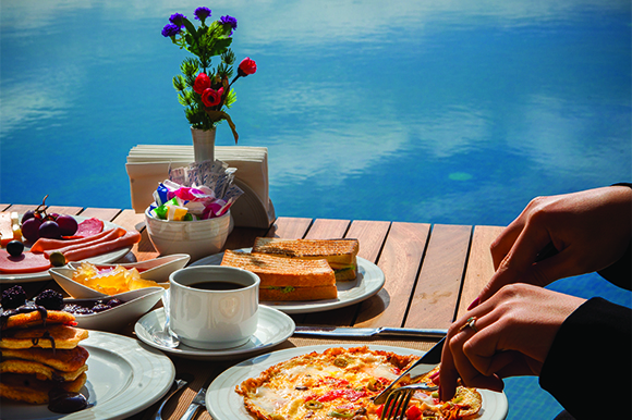 woman-eats-omelet-with-vegetables-pancakes-food-with-chocolate-cake-wooden-table